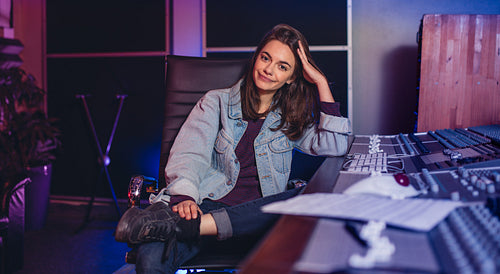 Female music composer sitting by sound mixing console