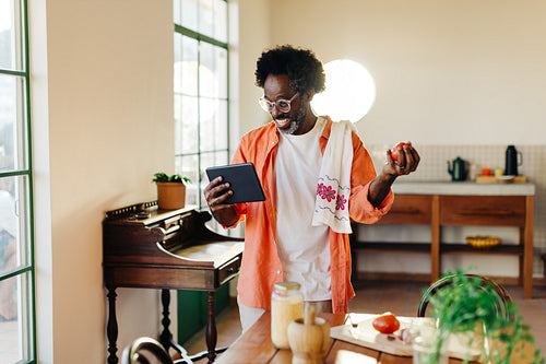 Happy Brazilian man cooking traditional breakfast with a touchscreen tablet in his home kitchen