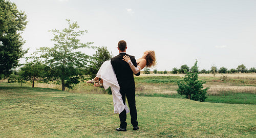 Bridegroom lifting up his bride at park