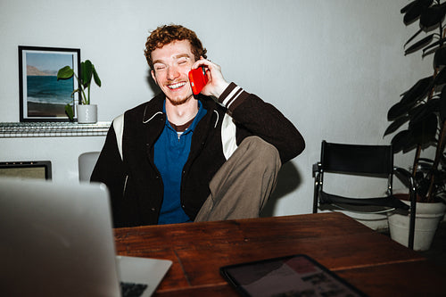 A man balances work and a phone call at his desk with a laptop nearby.