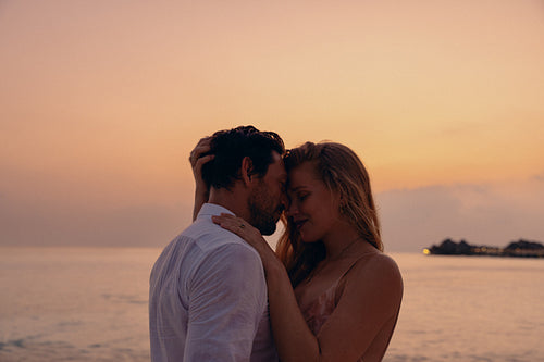 Affectionate couple sharing a tender moment during a luxury honeymoon at sunset on the beach
