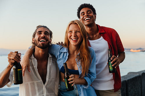 Joyful friends enjoying summer drinks at sunset by the sea