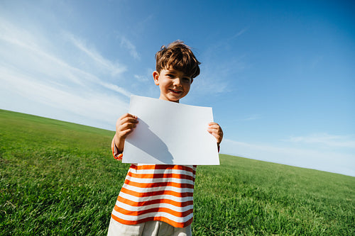 Boy holds blank paper in open field