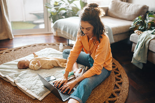 Mother working on laptop with baby at home