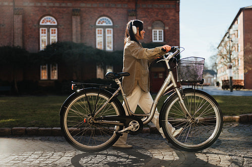 Woman walking bicycle through sunny urban courtyard