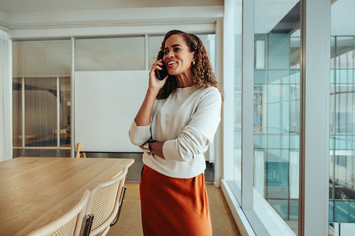 Professional multiracial woman enjoying a casual phone call in an office with large windows and natural light