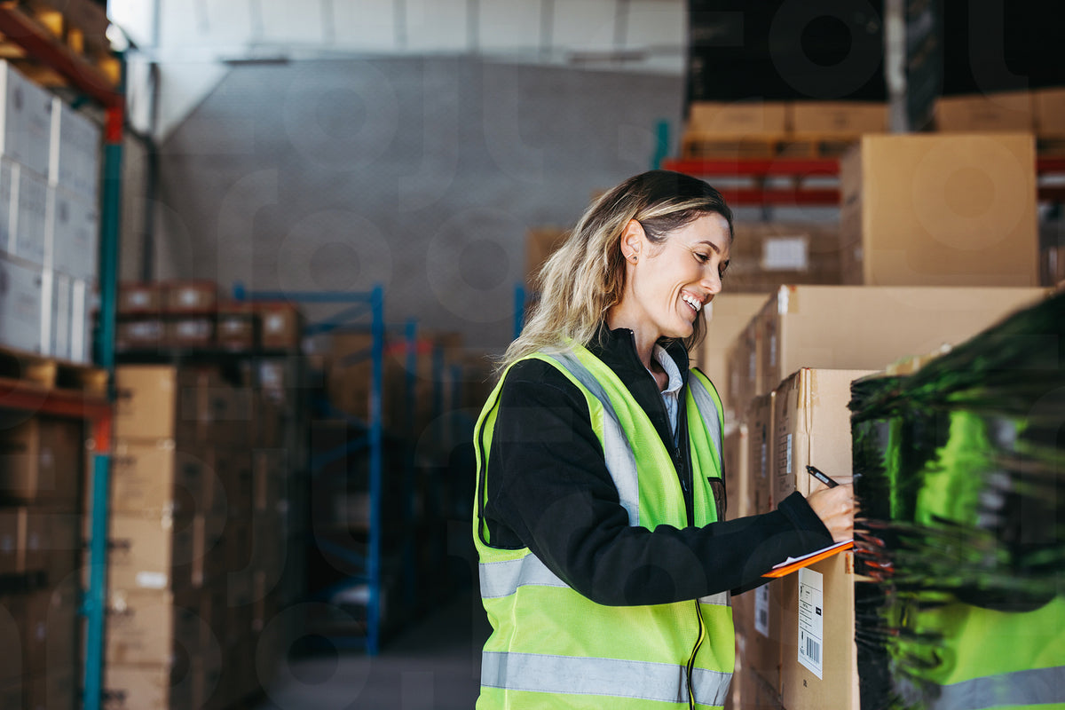 Happy warehouse manager writing on a clipboard in a logistics centre ...