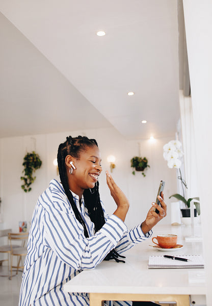 Happy young business woman waving on a video call while working in a coffee shop