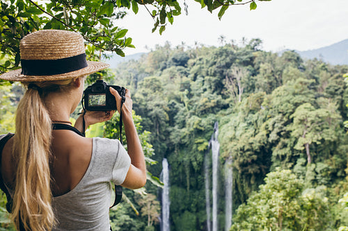 Female tourist photographing a waterfall in forest