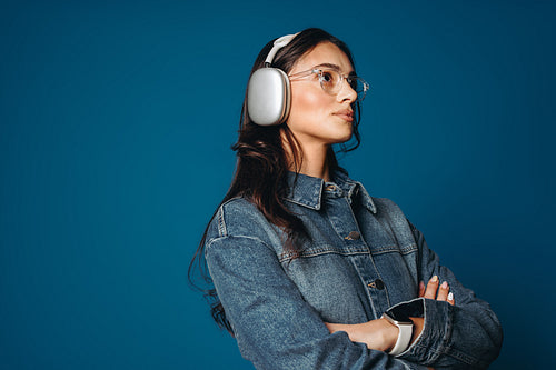 Woman wearing headphones in studio portrait with glasses against blue background