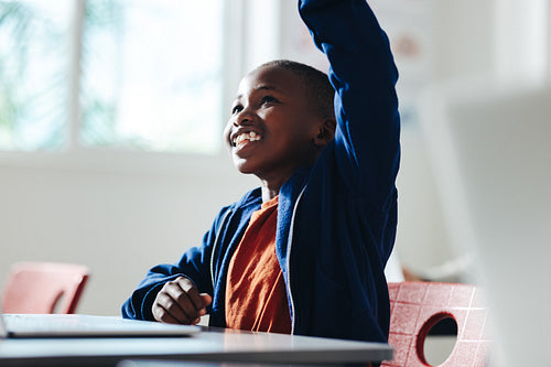 Smart young boy raising his hand to answer a question in a classroom