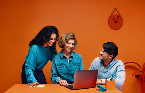 A strong creative team of adults brainstorming with a laptop in an office setting