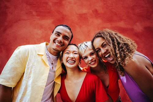Smiling with friends against a red wall in an outdoor group portrait