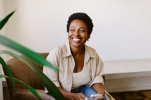 Black Brazilian woman smiling and using smartphone on sofa