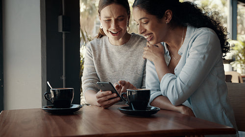Friends looking at mobile phone and laughing at a cafe