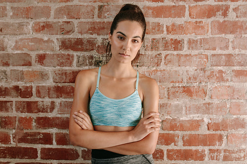 Beautiful young woman in sportswear against brick