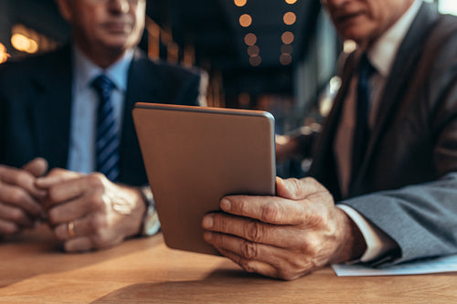 Digital tablet in hand of businessman talking to his partner