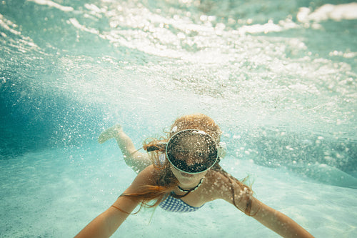 Girl swimming underwater during a vacation with snorkel mask and blue swimsuit