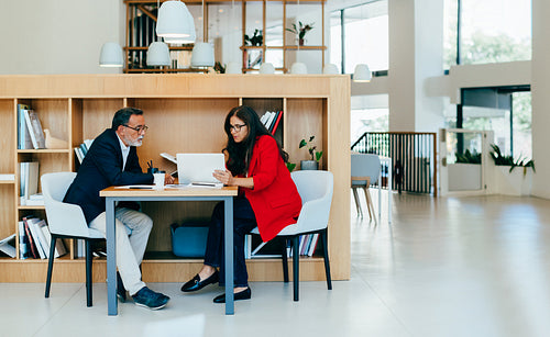 Two senior professionals discuss documents in a bright office environment