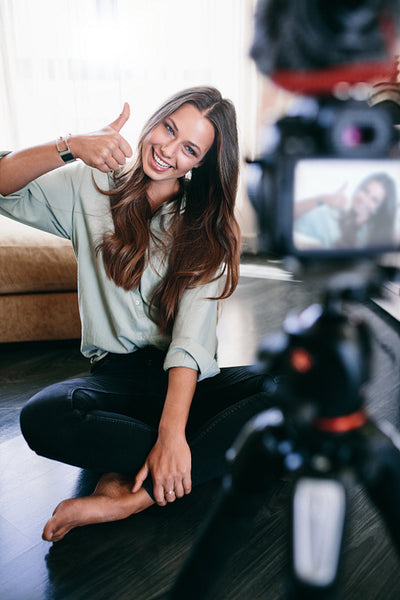 Beautiful girl recording video on tripod camera in her living room.
