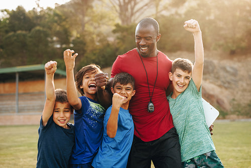 School kids celebrating with their coach in a sports ground