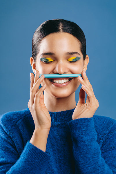 Beauty with graphic eyeliner: Happy young woman holding an eyeliner pen in a studio