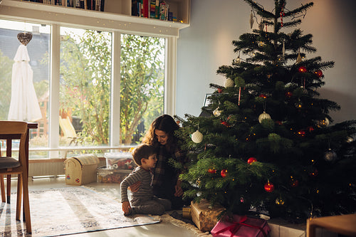Mother and son sitting by Christmas tree