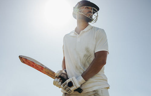 Male cricket player holding a bat under clear skies during a game