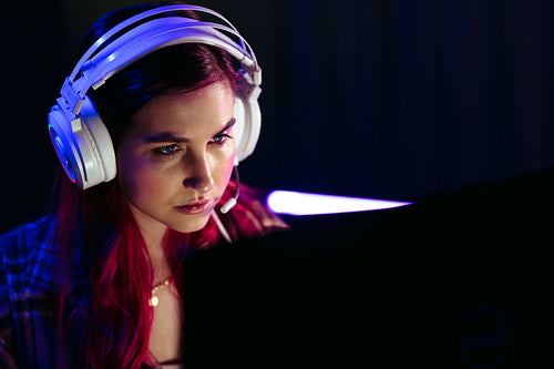 Girl playing a video game at night, sitting in front of her gaming pc with a headset