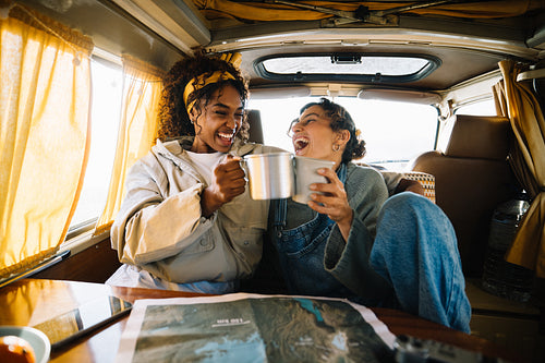 Friends share hot drinks in a cozy camper van on a sunny morning
