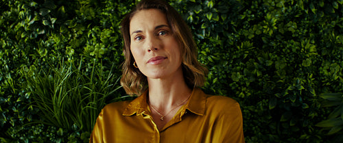 Confident businesswoman smiles in front of plant wall in office