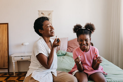 Mother and daughter applying lipstick together in a cozy bedroom