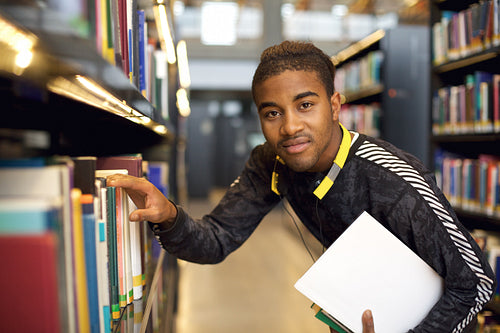 Young man getting books from a public library shelf