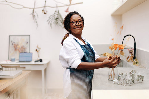 Mature florist arranging a bouquet of dry flowers in her flower shop