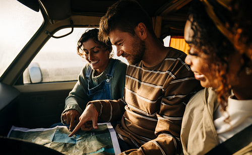 Three friends map reading inside a vehicle during a road trip adventure