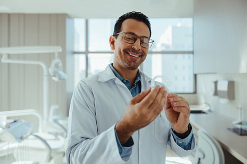Smiling male dentist presents aligner in modern clinic