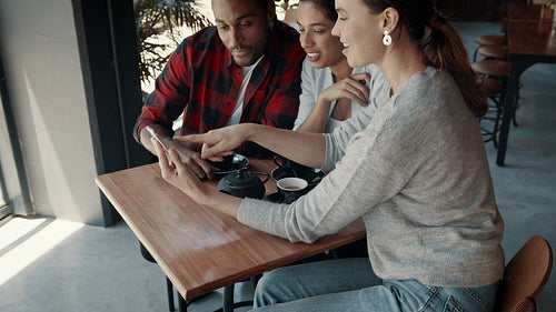 Friends looking at a mobile phone and having fun at a cafe