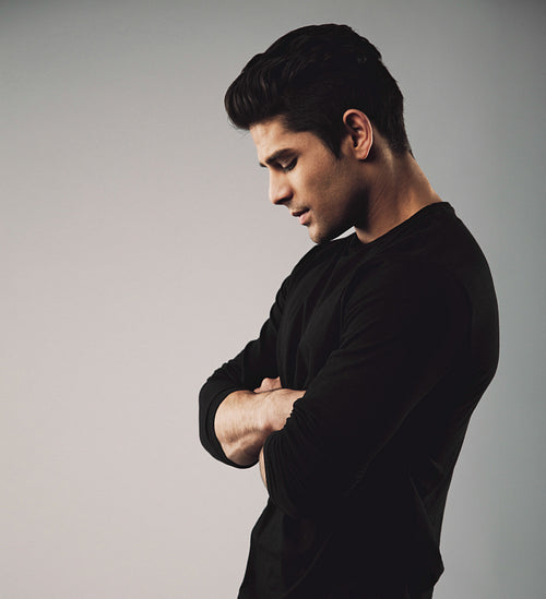Young man standing with arms crossed looking down
