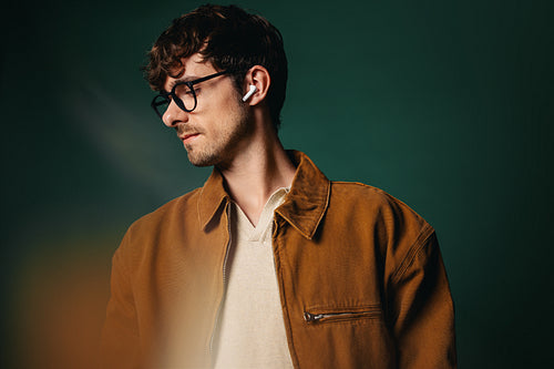 Glasses frame the man in a green studio portrait with earbuds