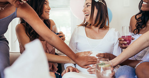 Smiling friends touching tummy of pregnant woman