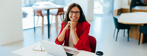 Professional woman in red blazer smiling at desk in a bright office