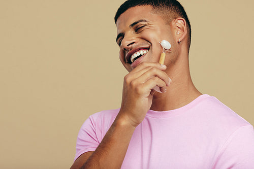 Man smiling as he massages his face with a jade roller stone in a studio