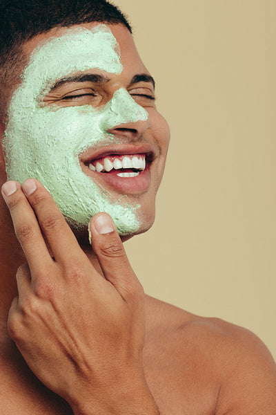 Man smiling as he cleanses his face with a green mask