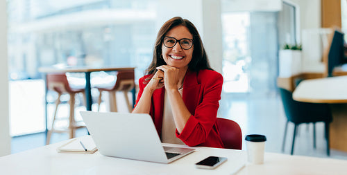 Confident businesswoman in red jacket smiling while working on a laptop