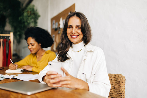 Happy business woman and fashion designer using a smartphone in her boutique office