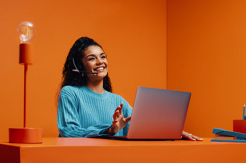 Customer service agent working with a laptop in orange monochromatic office