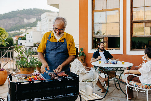 Man preparing churrasco during a family gathering on a sunny terrace