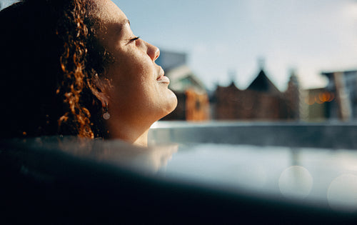 Peaceful woman basks in outdoor hot tub under afternoon sun