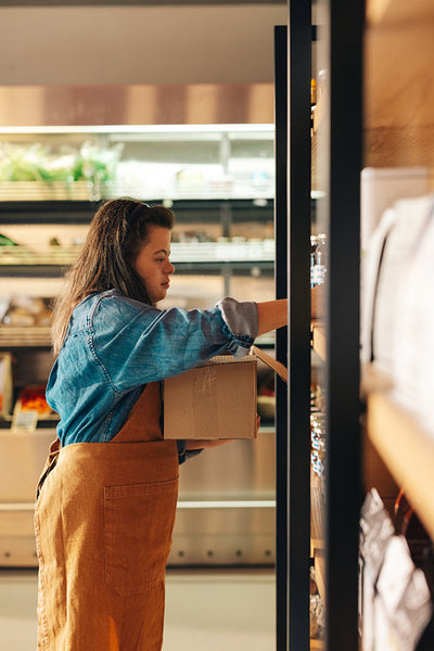 Grocery store worker with Down syndrome restocking food products in a shop