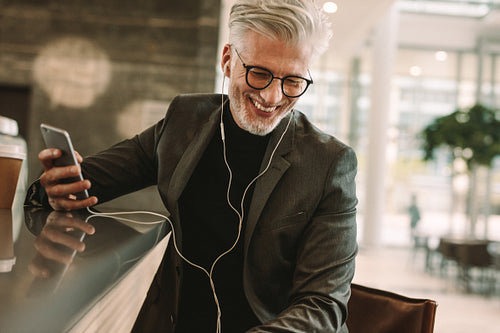 Smiling businessman in earphones and cellphone at cafe